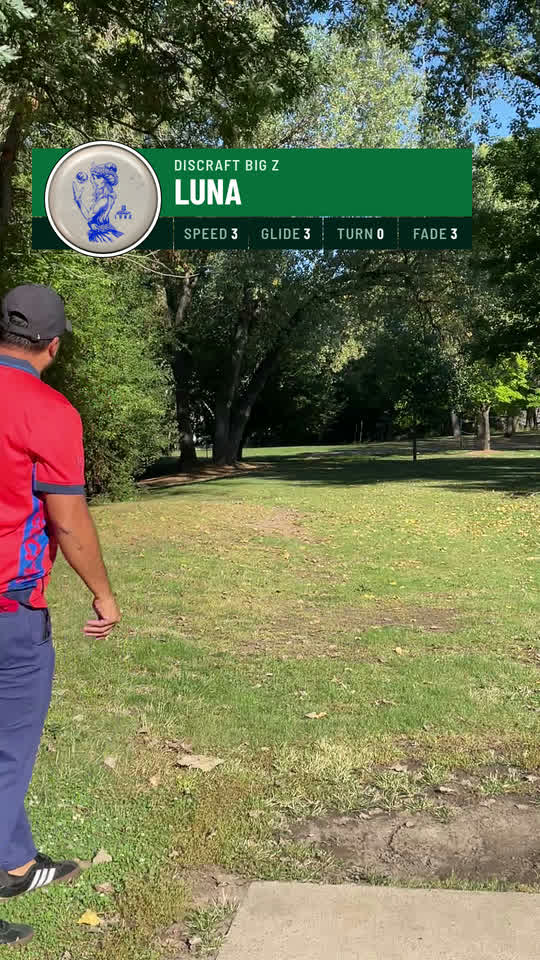 Selvin watching his drive fly at Alimagnet Park, with the disc overlay showing his white Discraft Big Z Luna as a round photo sticker beside its flight numbers.